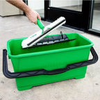 Tamis d’essorage en métal Unger pour seau de vitrier 28L, outil de nettoyage pour vitres, dans une main avec seau.